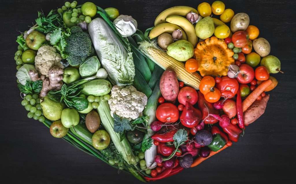 Heart made of fresh vegetables and fruit on wooden background, top view.